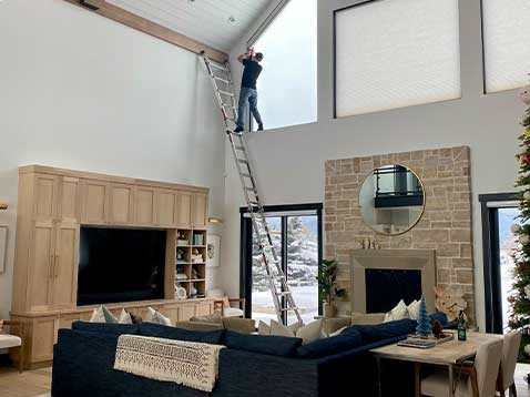 Man on a ladder installing window coverings
